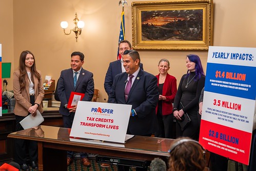 Asm. González standing behind desk with sign on desk