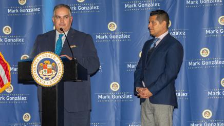 Speaker Emeritus Pérez at podium, speaking as former assemblymember Miguel Santiago listens on