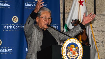 Guest speaker at podium, speaking and holding up both arms