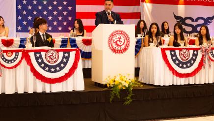 Asm. González at podium, speaking, with honorees at either side and in background