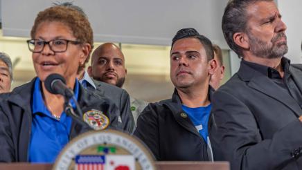 Asm. González listens on as Mayor Bass speaks at podium