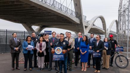 Asm. González at podium, speaking, as others listen on