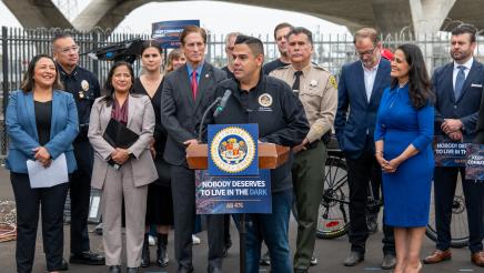 Asm. González at podium, speaking, as others listen on
