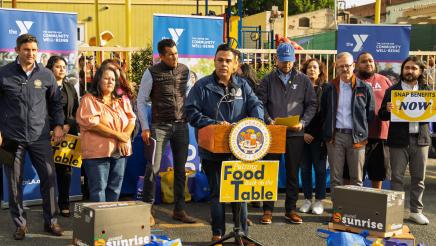 Wide view of Asm. González at podium, speaking, as Speaker Rivas and others listen on